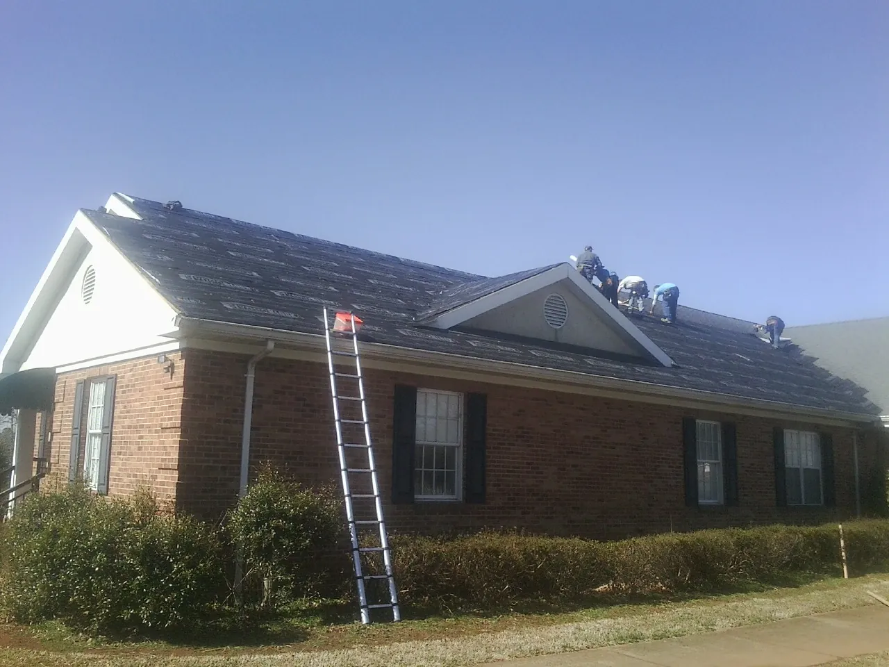 Crew tearing shingles off a brick ranch roof with a ladder set — Metal Roof Repair work by our crew in Sugar Grove