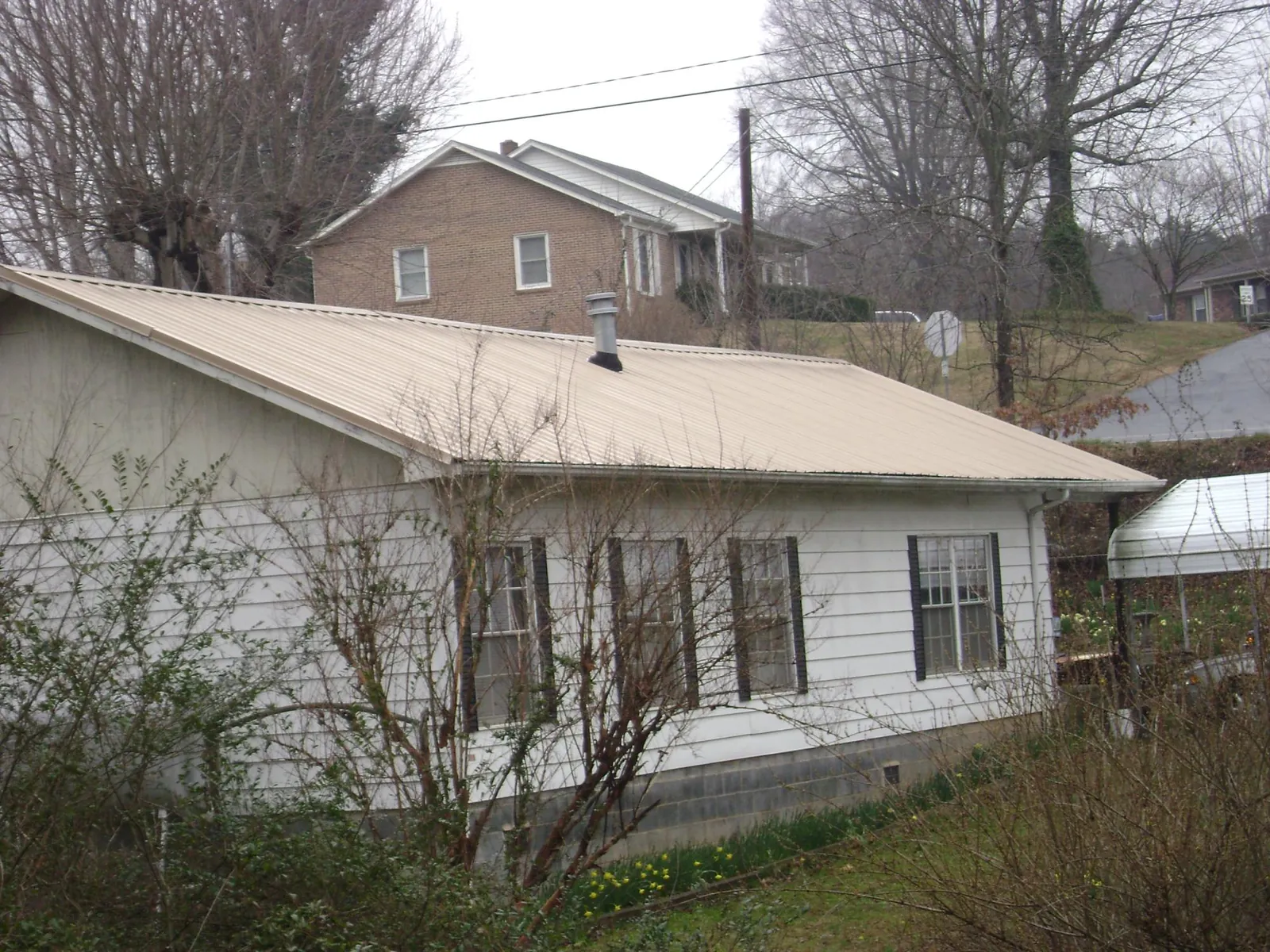 Tan metal roof on a white sided house set into a hillside — Commercial Roofing by Roofing Brothers in Sugar Grove